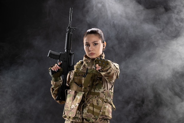 Vista frontale della soldatessa in uniforme con il fucile sul muro nero