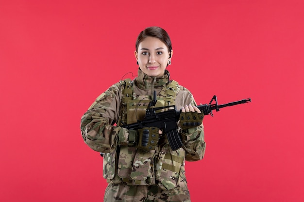 Vista frontale della soldatessa in uniforme militare con la parete rossa della mitragliatrice