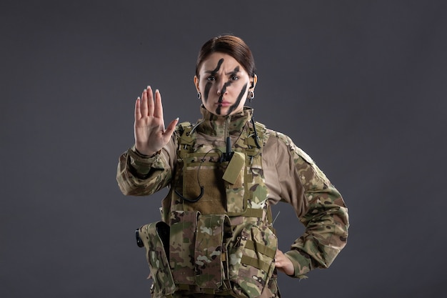 Vista frontale della soldatessa in uniforme militare sul muro scuro