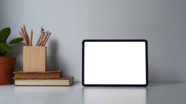 Vista frontale della tavoletta digitale con pianta del libro dello schermo vuota e portamatite sul tavolo bianco