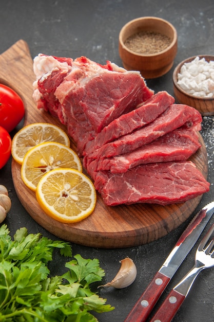 Vista frontale di carne fresca affettata con fette di limone e verdure su sfondo grigio scuro cibo per animali barbecue macellaio pasto carne colore cena