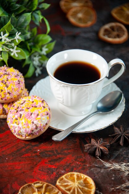 Vista frontale di deliziosi biscotti di zucchero e una tazza di caffè con fettine di limone essiccate su sfondo scuro di colori misti