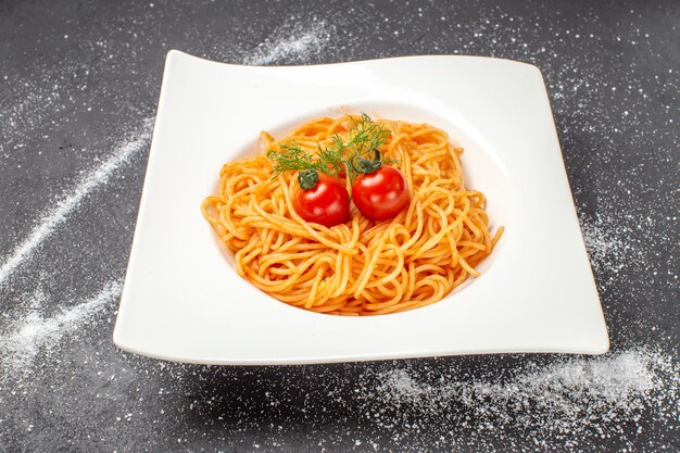 Vista frontale di deliziosi spagetty serviti con pomodori verdi su un piatto a forma quadrata su sfondo bianco nero