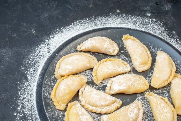 Vista frontale di gnocchi crudi fatti in casa su un piatto blu sul lato sinistro sulla parete nera