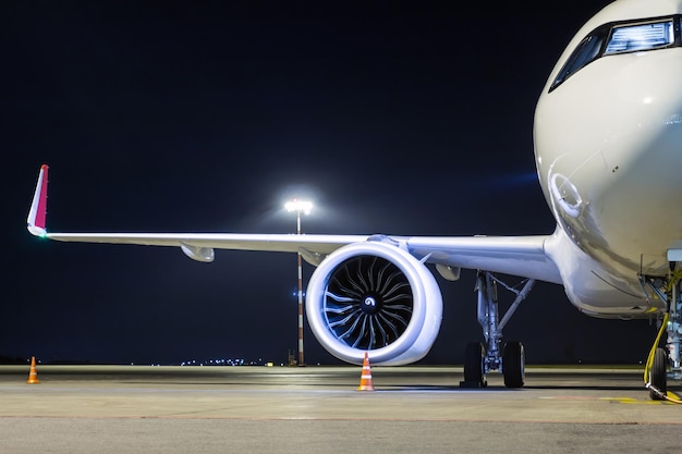 Vista frontale di un aereo passeggeri bianco collegato a un alimentatore esterno su un grembiule notturno dell'aeroporto