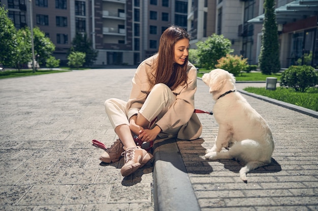 Vista frontale di un'allegra giovane bella signora dai capelli scuri che sorride al suo amico a quattro zampe all'aperto