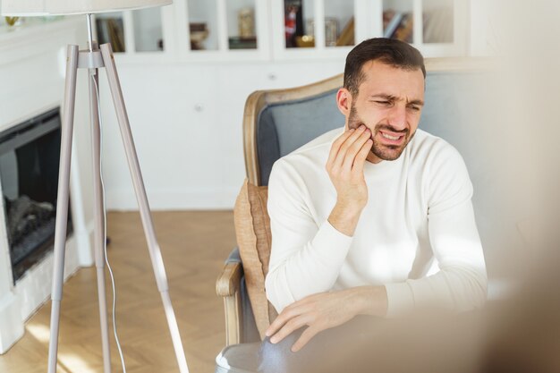 Vista frontale di un maschio caucasico dai capelli scuri che soffre di un dolore dentale acuto a casa