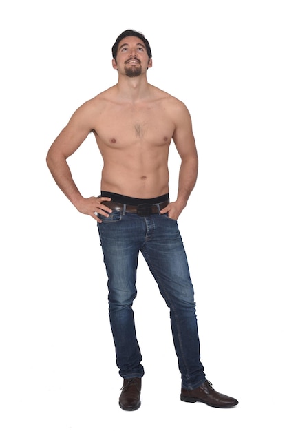 Vista frontale di un uomo a torso nudo e con jeans blu che guarda in alto su sfondo bianco