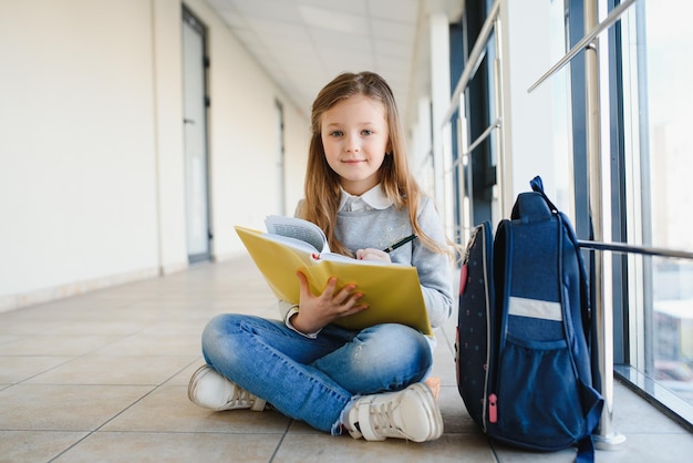 Vista frontale di una bella ragazza bionda con in mano molti libri e appunti colorati Ragazza adolescente intelligente che sorride alla telecamera in piedi sul corridoio della scuola internazionale