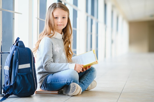 Vista frontale di una bella ragazza bionda con in mano molti libri e appunti colorati Ragazza adolescente intelligente che sorride alla telecamera in piedi sul corridoio della scuola internazionale