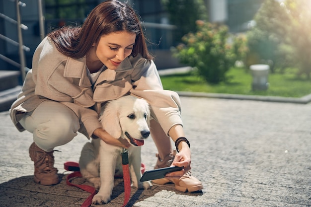 Vista frontale di una bella signora e del suo cane in posa per la fotocamera del cellulare all'aperto