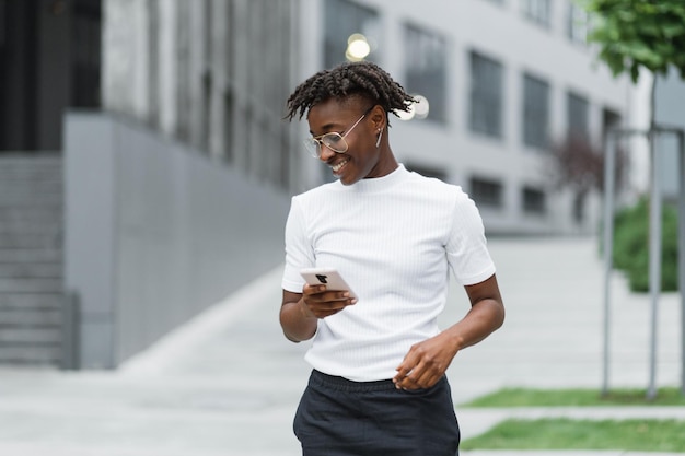 Vista frontale di una donna africana d'affari piacevole che utilizza uno smartphone moderno mentre si trova all'aperto