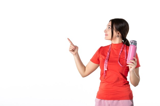 Vista frontale di una giovane ragazza concentrata in camicetta rossa che tiene il misuratore e mostra il termos rivolto verso l'alto su sfondo bianco