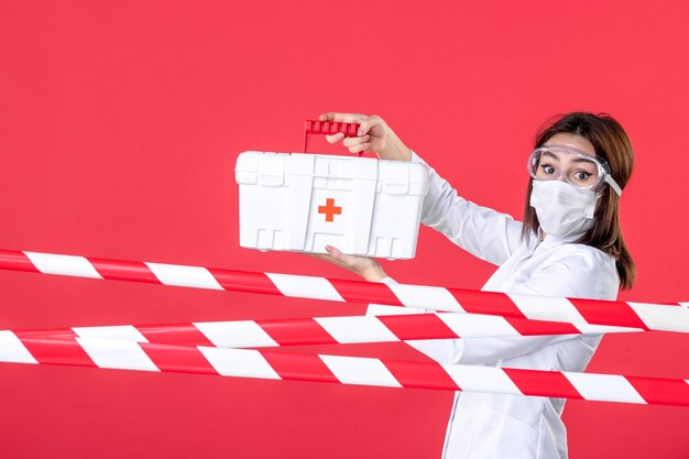 vista frontale dottoressa che tiene il kit di pronto soccorso sullo sfondo rosso linea sanitaria virus covid crimine ospedale pericolo cura sigillata