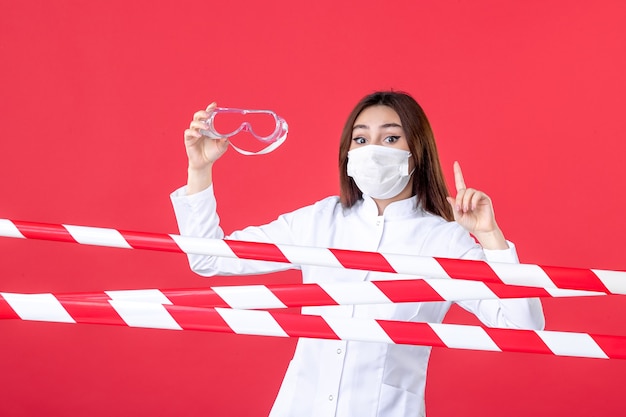 vista frontale dottoressa in maschera con occhiali da sole protettivi sullo sfondo rosso criminalità salute ospedale linea virus covid medico sigillato