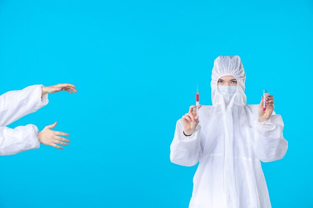 vista frontale dottoressa in tuta protettiva e maschera che tiene l'iniezione su sfondo blu ospedale medico covid pandemia virus salute