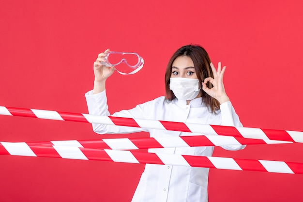 vista frontale dottoressa in uniforme medica e maschera con occhiali da sole protettivi su sfondo rosso crimine linea ospedaliera virus covid sigillato