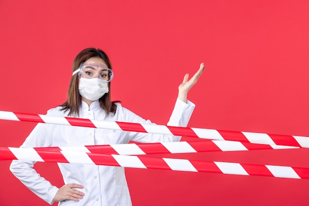 vista frontale dottoressa in uniforme medica e maschera su sfondo rosso crimine sigillato covid- ospedale linea medica isolamento salute