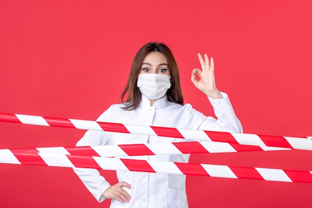 vista frontale dottoressa in uniforme medica e maschera su sfondo rosso linea pandemica sigillata covid- virus sanitario crimine ospedaliero