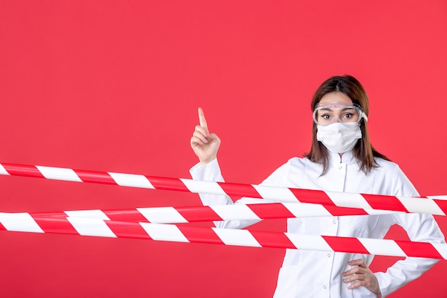 vista frontale dottoressa in uniforme medica e maschera sullo sfondo rosso virus della linea criminale sigillata covid- ospedale sanitario medico