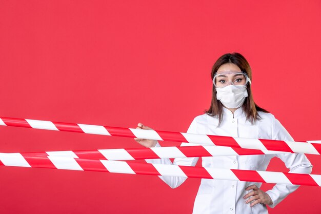 vista frontale dottoressa in uniforme medica e maschera sullo sfondo rosso virus della linea criminale sigillata covid- ospedale sanitario medico