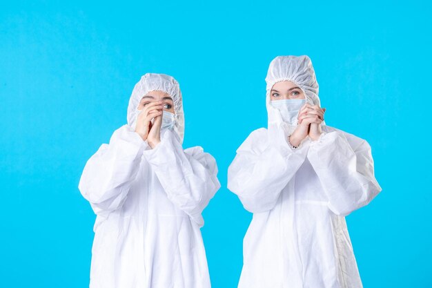 vista frontale dottoresse in tute protettive e maschera su sfondo blu colori virus pandemia ospedale scienza sanitaria covid-