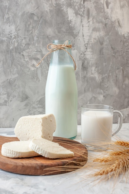 vista frontale fette di formaggio bianco su tavola di legno bottiglia di latte tazza di latte spighe di grano sul tavolo