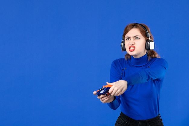 vista frontale giocatore femminile che gioca al videogioco con gamepad e cuffie su sfondo blu giocatore ragazza video per adulti vincendo gioia giovanile giovane divano