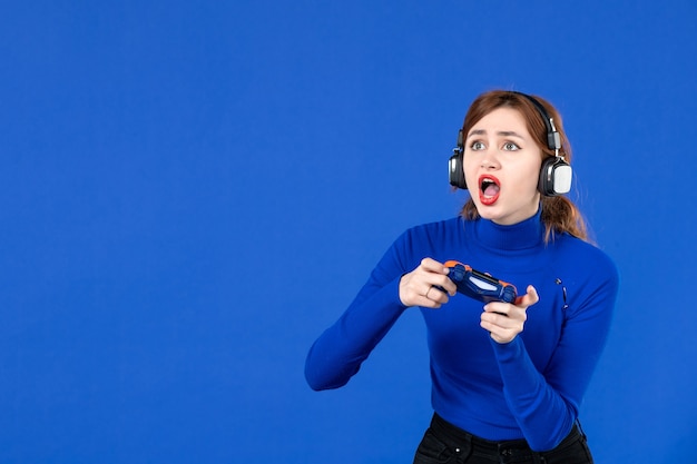 vista frontale giocatore femminile che gioca al videogioco con gamepad e cuffie su sfondo blu giocatore ragazza video per adulti vincendo giovinezza gioia virtuale giovane divano