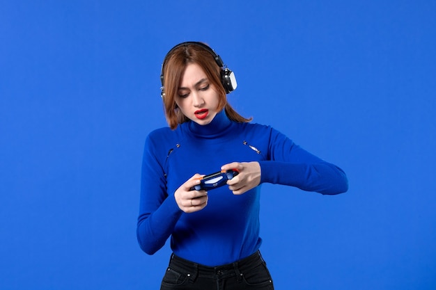 vista frontale giocatore femminile con cuffie e gamepad che gioca a un videogioco su sfondo blu ragazza giovane divano vincente giocatore video adulto gioia virtuale giovane