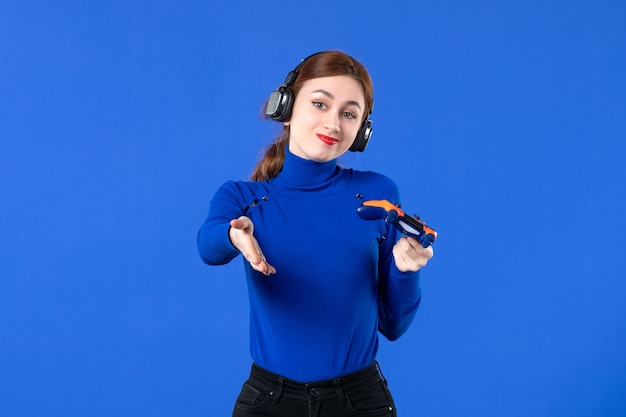 vista frontale giocatore femminile con cuffie e gamepad che gioca al videogioco su sfondo blu divano giocatore adulto gioia ragazza giovane video vincente virtuale