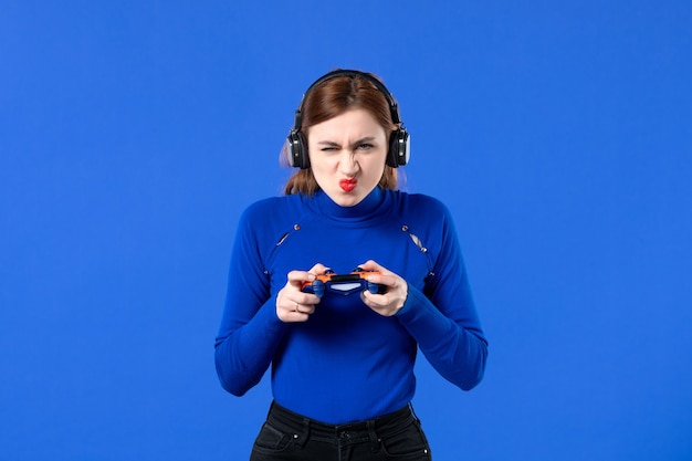 vista frontale giocatore femminile con cuffie e gamepad su sfondo blu divano video ragazza adulta giovane giocatore vincente gioia virtuale