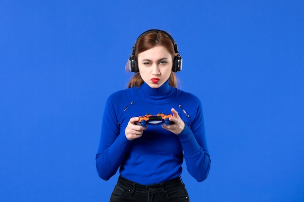 vista frontale giocatore femminile con cuffie e gamepad su sfondo blu divano video ragazza adulta giovani giocatori vincenti gioia giovanile virtuale