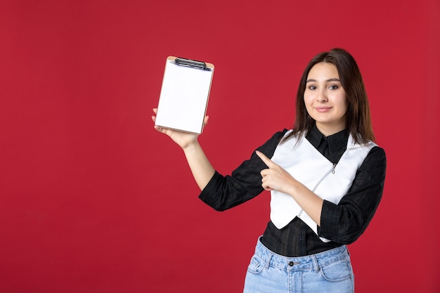 vista frontale giovane bella cameriera in uniforme che tiene nota di file per ordini su sfondo rosso lavoro bellezza donna lavoro lavoratore cibo cena serate