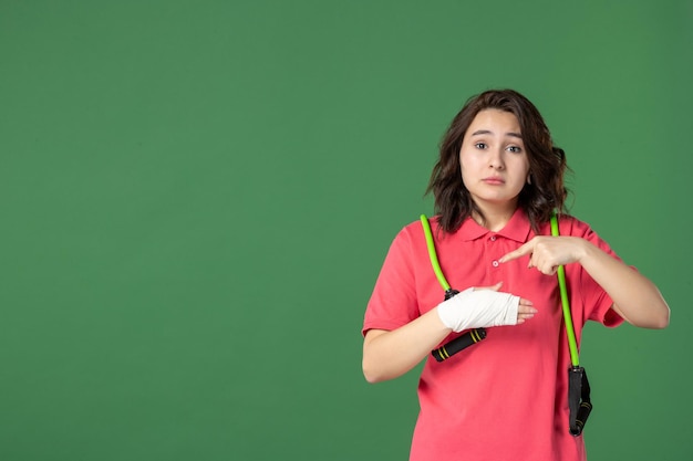 Vista frontale giovane bella commessa con la fasciatura sulla mano ferita su una superficie verde