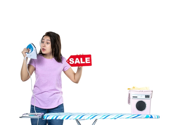 Vista frontale giovane casalinga azienda red vendita scrittura e ferro da stiro su sfondo bianco lavoro domestico secco shopping vestiti macchina color