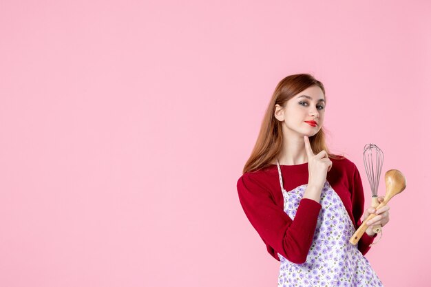 vista frontale giovane casalinga in posa con frusta e cucchiaio di legno su sfondo rosa donna torta professione pasta cucina orizzontale torta uniforme