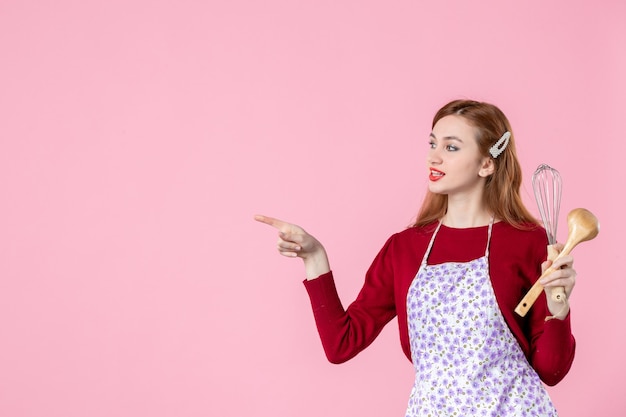 vista frontale giovane casalinga in posa con frusta e cucchiaio di legno su sfondo rosa donna torta torta professione uniforme cucina orizzontale cucinare