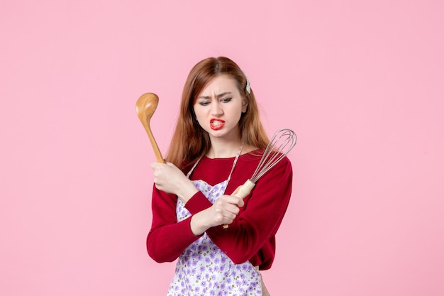 vista frontale giovane casalinga in posa con frusta e cucchiaio di legno su sfondo rosa professione cucina torta di pasta donna torta cucina orizzontale