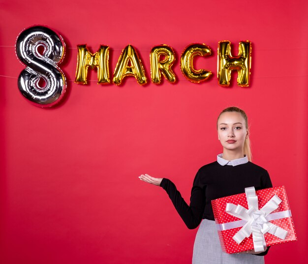 vista frontale giovane donna che tiene presente con decorazione di marzo su sfondo rosso salone passione shopping femminile giorno della donna uguaglianza denaro lussuoso
