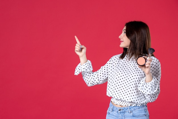 Vista frontale giovane donna con nappa in polvere per il trucco e sul muro rosso