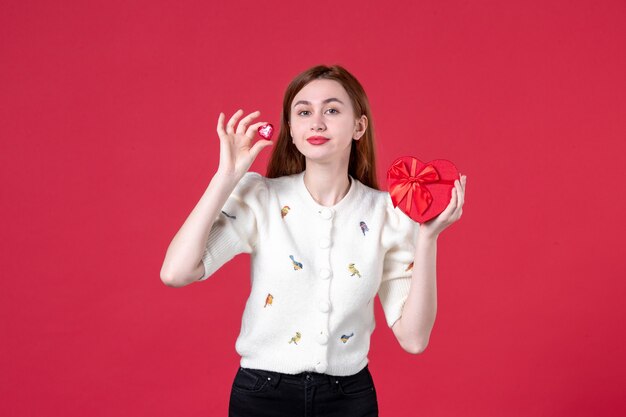 vista frontale giovane femmina che tiene regalo a forma di cuore rosso su sfondo rosso festa della donna sensuale femminile marcia matrimonio uguaglianza amore moda shopping
