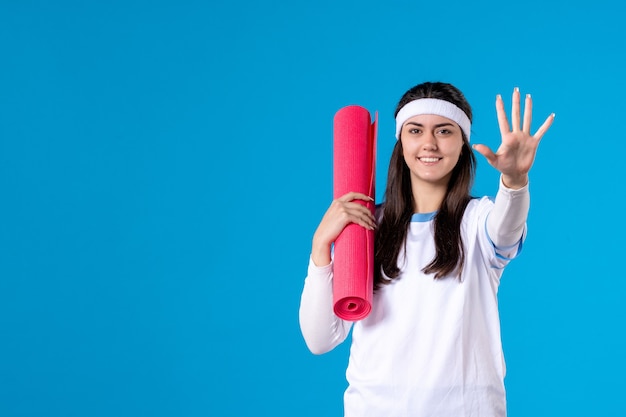 Vista frontale giovane femmina con materassino yoga sulla parete blu