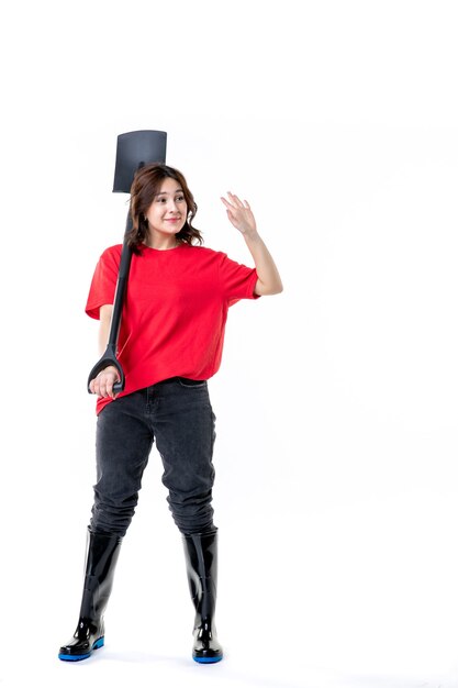 vista frontale giovane femmina in maglietta rossa tenendo la pala nera su sfondo bianco suolo lavoro donna lavoro cimitero terra emozione natura