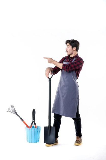 Vista frontale giovane giardiniere maschio con pala nera su sfondo bianco terreno uniforme lavoro lavoro giardino fiorito terreno di scavo