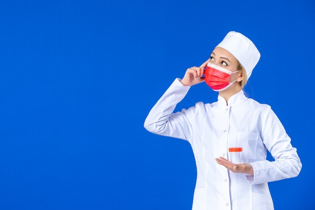 vista frontale giovane infermiera in tuta medica con maschera che tiene il pallone su sfondo blu virus ospedaliero covid- medicina sanitaria farmaco vaccino pandemico