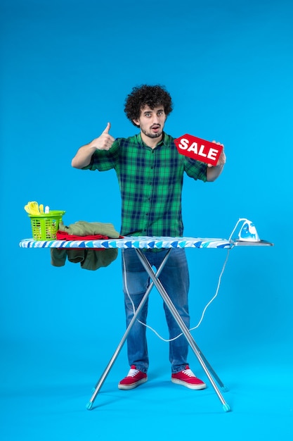 Vista frontale giovane maschio azienda vendita iscritto su sfondo blu casa lavatrice colore pulito shopping lavori domestici