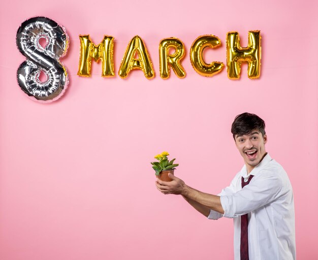 Vista frontale giovane maschio che dà a qualcuno un piccolo fiore come presente di marzo su sfondo rosa uomo festa uguaglianza femminile festa della donna matrimonio colore vacanza