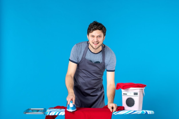 Vista frontale giovane maschio che si prepara a stirare su sfondo blu stirare vestiti uomo lavatrice pulizia lavanderia lavori domestici