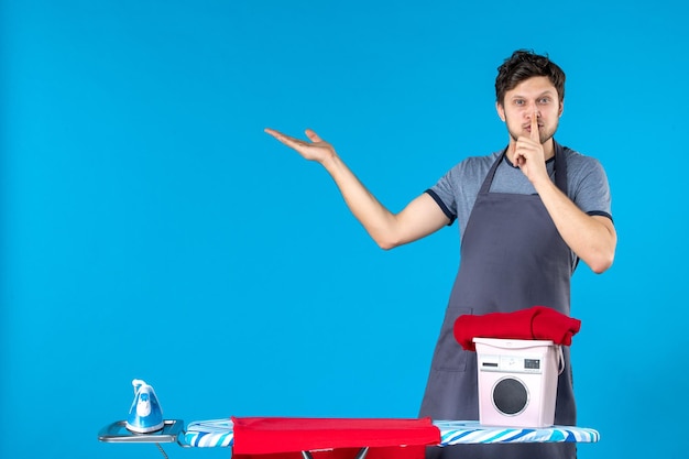 Vista frontale giovane maschio con asse da stiro che chiede di tacere su sfondo blu ferro colore uomo lavatrice lavanderia lavori domestici pulizia